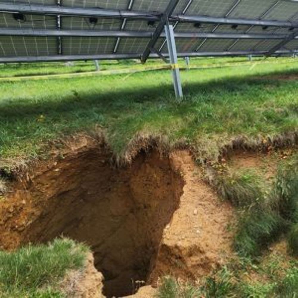 Solar panels above a large erosion hole in grassy terrain, highlighting land instability issues.